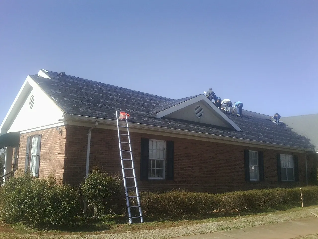 Crew tearing shingles off a brick ranch roof with a ladder set — Metal Roof Repair work by our crew in Dwight