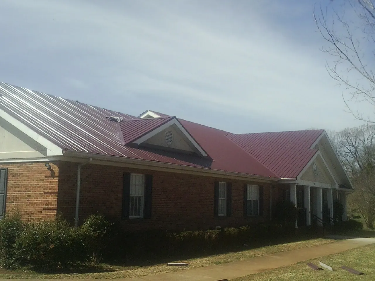 Red metal roof with gabled entries on a long brick building, from a Hail Damage Roof Repair job in Dwight
