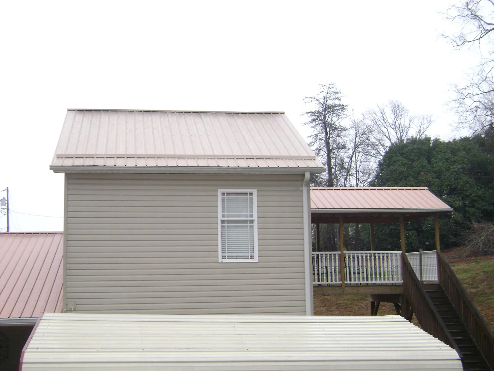 Tan metal roofs on a two story addition and attached porch, from a Roof Replacement job in Dwight